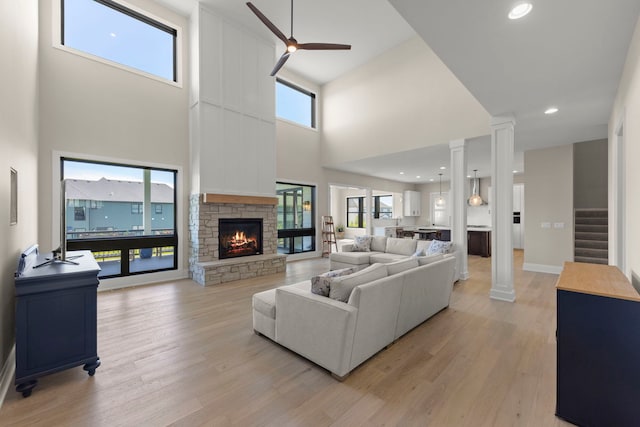 4216 Carpenter Rd, Naperville, IL 60564 - living room with a stone fireplace, ceiling fan, a high ceiling, light wood-type flooring, and decorative columns