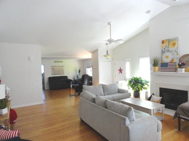 living room featuring wood finished floors, healthy amount of natural light, a ceiling fan, a fireplace with flush hearth, and high vaulted ceiling