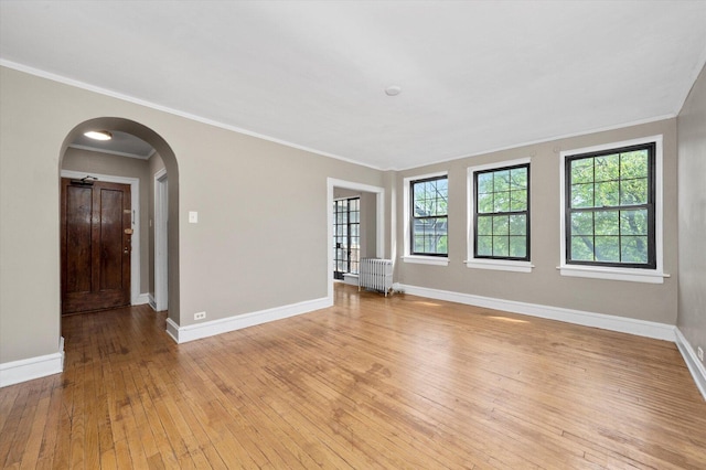 3017 E 78th St Unit 4B, Chicago, IL 60649 - empty room featuring radiator heating unit, light wood finished floors, arched walkways, and crown molding