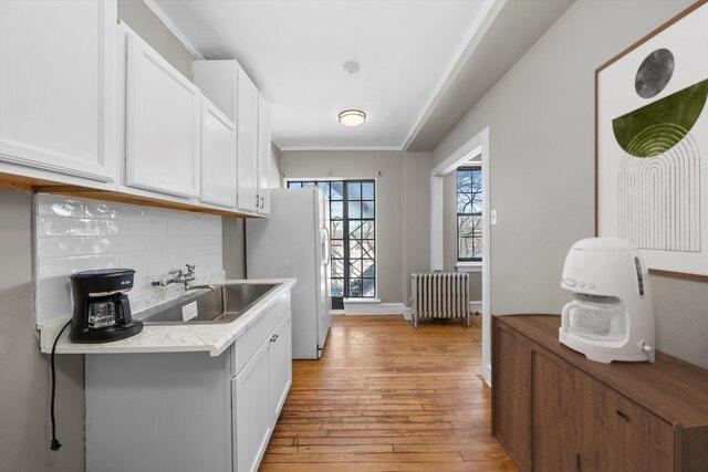 3017 E 78th St Unit 4B, Chicago, IL 60649 - kitchen with radiator, light wood-style flooring, freestanding refrigerator, and white cabinetry