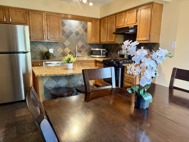 26296 N Green St Unit 5C, Mundelein, IL 60060 - kitchen featuring stainless steel appliances, under cabinet range hood, decorative backsplash, and brown cabinetry