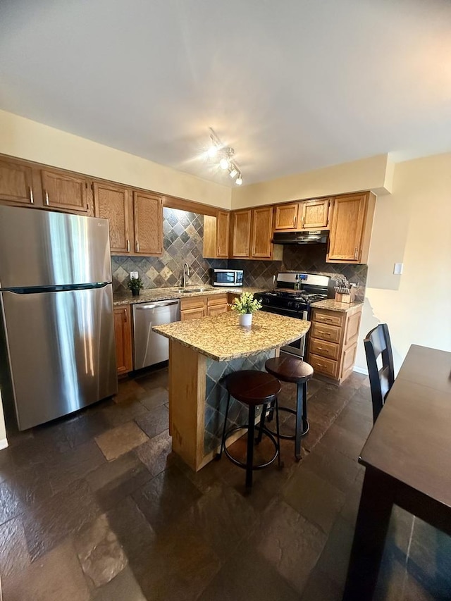 26296 N Green St Unit 5C, Mundelein, IL 60060 - kitchen featuring appliances with stainless steel finishes, under cabinet range hood, tasteful backsplash, and a kitchen island
