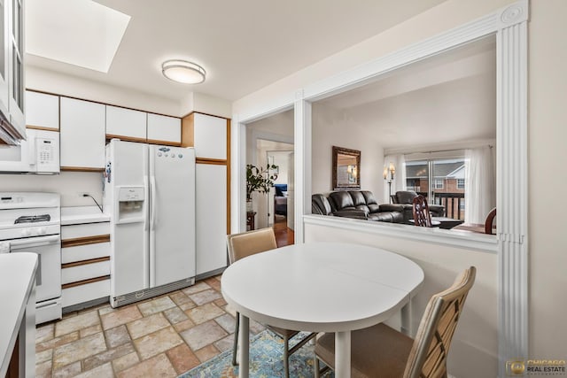 6561 W School Ave Unit 305C, Chicago, IL 60634 - kitchen featuring white appliances, white cabinetry, light stone finish floors, a skylight, and light countertops