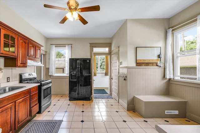 301 N Main St, Fithian, IL 61844 - kitchen featuring black refrigerator with ice dispenser, stainless steel range with gas stovetop, under cabinet range hood, a wainscoted wall, and light countertops