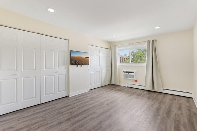 9250 Noel Ave Unit 205E, Des Plaines, IL 60016 - unfurnished bedroom with multiple closets, a baseboard heating unit, a wall mounted air conditioner, wood finished floors, and recessed lighting