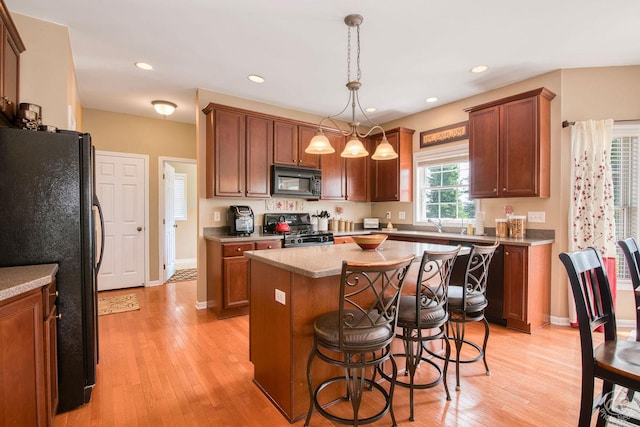 414 Alden Dr, Sycamore, IL 60178 - kitchen with black appliances, light wood-style flooring, a kitchen island, a kitchen bar, and decorative light fixtures