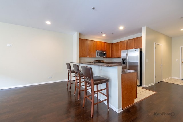 915 S Oak Park Ave Unit 1B, Oak Park, IL 60304 - kitchen featuring stainless steel appliances, wood finished floors, a kitchen breakfast bar, dark stone counters, and brown cabinetry