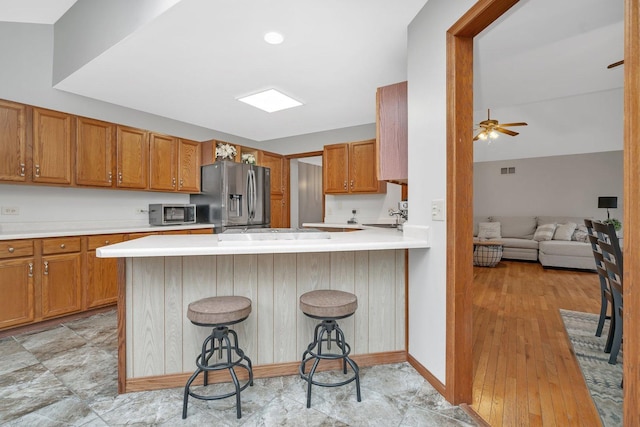 5209 Meadowbrook St, Plainfield, IL 60586 - kitchen featuring stainless steel appliances, light countertops, brown cabinetry, a peninsula, and a breakfast bar