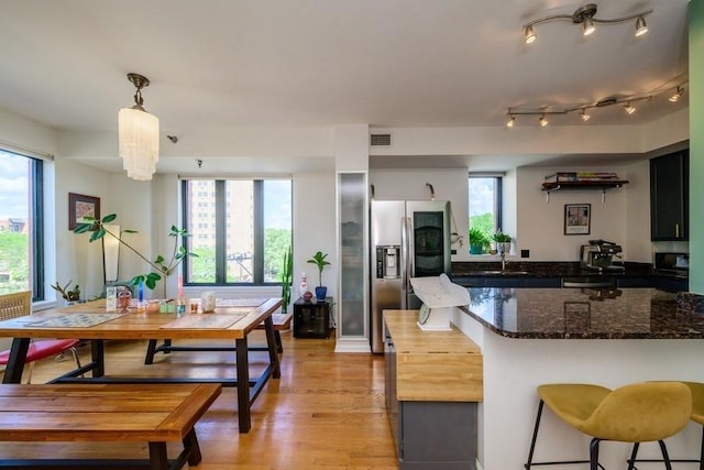 3232 N Halsted St Unit D412, Chicago, IL 60657 - kitchen featuring stainless steel appliances, light wood-style flooring, dark stone countertops, a breakfast bar, and decorative light fixtures