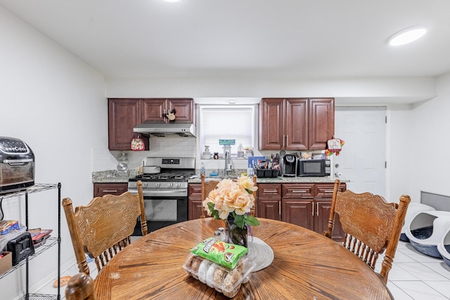 2958 S Lowe Ave, Chicago, IL 60616 - kitchen featuring stainless steel range with gas cooktop, under cabinet range hood, black microwave, backsplash, and light tile patterned floors