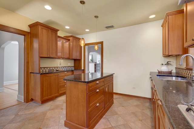 3838 Johnson Ave, Western Springs, IL 60558 - kitchen with arched walkways, dark stone counters, brown cabinetry, a kitchen island, and pendant lighting