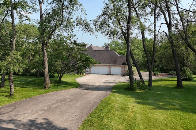 view of front of property featuring driveway, an attached garage, a front lawn, a chimney, and a shingled roof