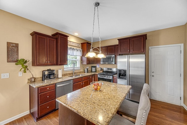 504 W Hillcrest Dr, Romeoville, IL 60446 - kitchen featuring appliances with stainless steel finishes, light wood finished floors, a kitchen island, light stone counters, and decorative light fixtures