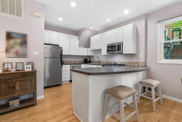 2809 N Wolcott Ave Unit H, Chicago, IL 60657 - kitchen with stainless steel appliances, a peninsula, light wood-style flooring, dark countertops, and white cabinetry