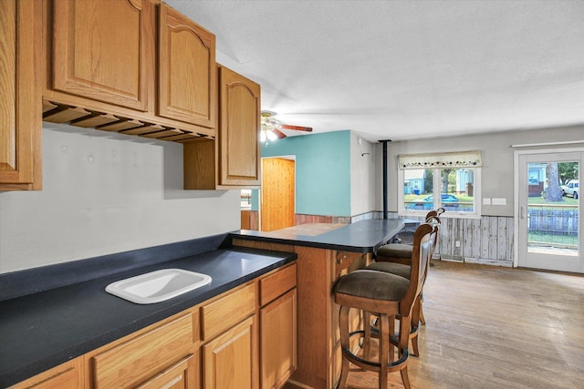 403 E Cooke St, Mount Pulaski, IL 62548 - kitchen featuring dark countertops, a breakfast bar area, light wood finished floors, ceiling fan, and brown cabinetry