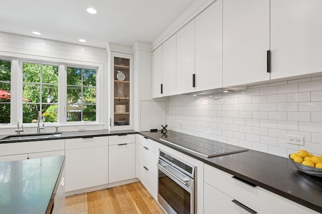 624 Laurel Ave, Wilmette, IL 60091 - kitchen featuring oven, black electric stovetop, dark countertops, light wood-type flooring, and backsplash