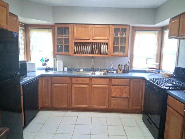 kitchen with black appliances, brown cabinets, glass insert cabinets, light tile patterned floors, and dark countertops