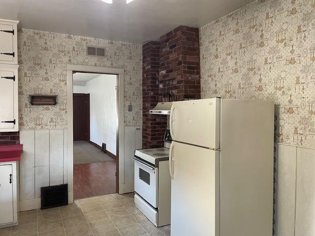 1322 N Prairie Ave, Joliet, IL 60435 - kitchen with white appliances, extractor fan, light tile patterned floors, wallpapered walls, and white cabinets
