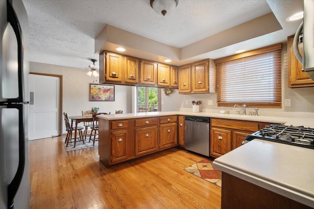 2210 Hedgewood Dr, Bloomington, IL 61704 - kitchen with stainless steel appliances, brown cabinets, a peninsula, a textured ceiling, and light wood-type flooring