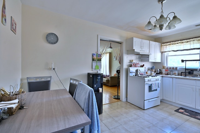 kitchen with white gas range oven, a chandelier, under cabinet range hood, white cabinetry, and light tile patterned floors