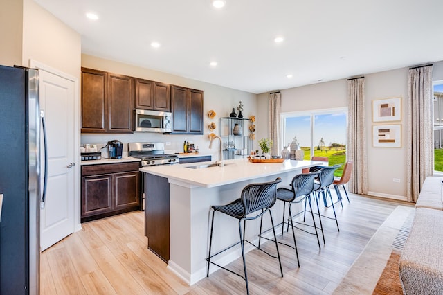 12003 Jordi Rd, Huntley, IL 60142 - kitchen featuring appliances with stainless steel finishes, light wood finished floors, light countertops, a kitchen bar, and a center island with sink