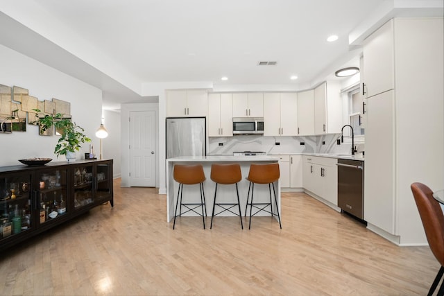 1225 N Paulina St Unit 3S, Chicago, IL 60622 - kitchen with stainless steel appliances, a breakfast bar, white cabinetry, light wood-style flooring, and light countertops