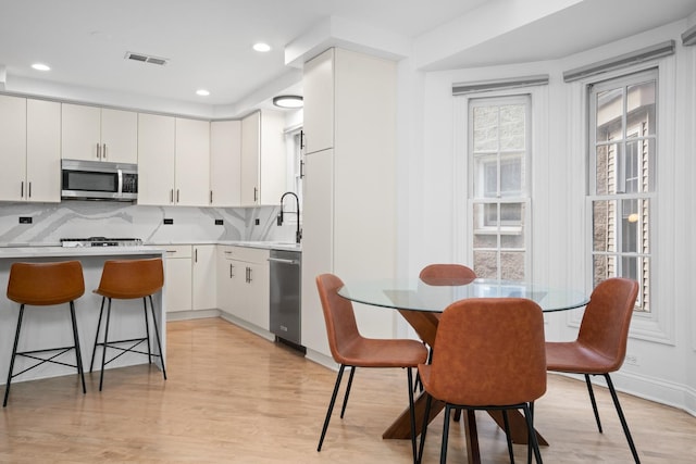 1225 N Paulina St Unit 3S, Chicago, IL 60622 - kitchen with stainless steel appliances, light wood-type flooring, tasteful backsplash, a kitchen breakfast bar, and white cabinets