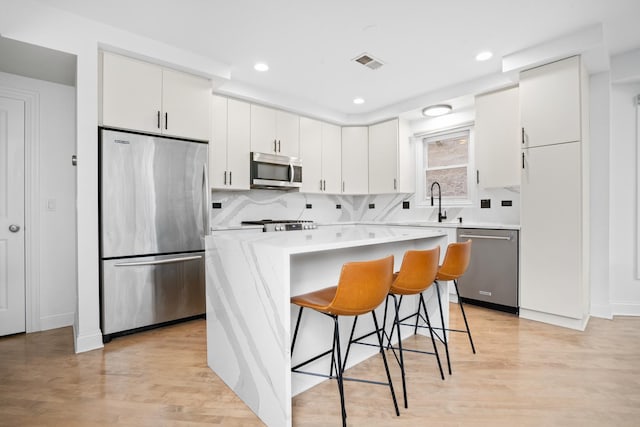 1225 N Paulina St Unit 3S, Chicago, IL 60622 - kitchen with stainless steel appliances, a breakfast bar area, light wood-style flooring, white cabinetry, and recessed lighting