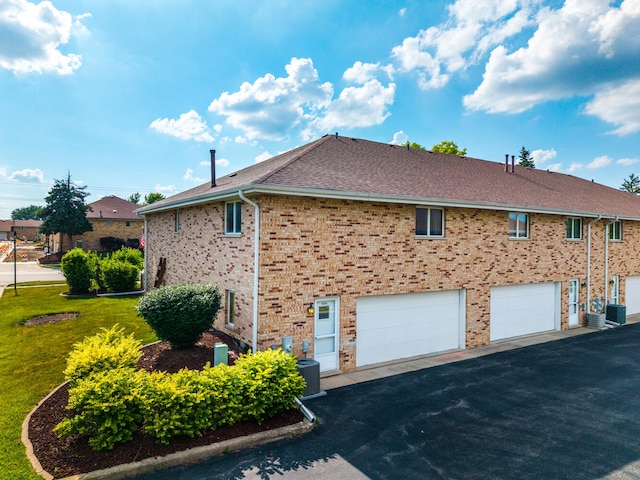 15317 S 73rd Ave Unit 8, Orland Park, IL 60462 - view of side of home featuring asphalt driveway, an attached garage, brick siding, a shingled roof, and a yard