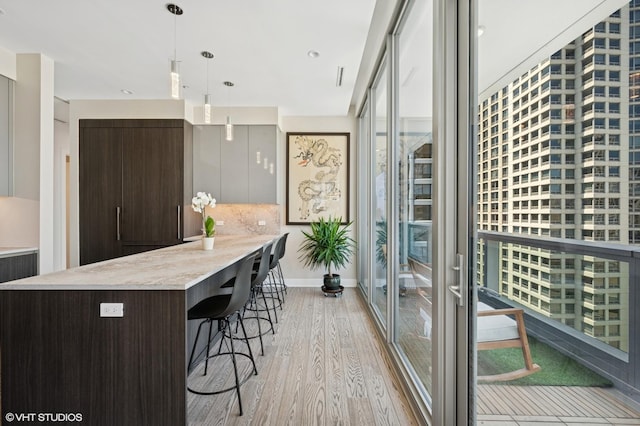 403 N Wabash Ave Unit 17C, Chicago, IL 60611 - kitchen with light wood-type flooring, light countertops, dark brown cabinetry, a breakfast bar, and decorative light fixtures