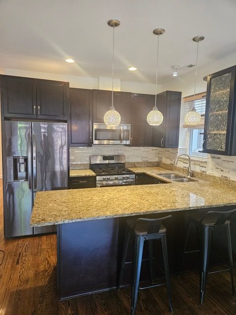 2447 W Walton St Unit 2, Chicago, IL 60622 - kitchen featuring stainless steel appliances, light stone counters, a peninsula, decorative light fixtures, and a breakfast bar