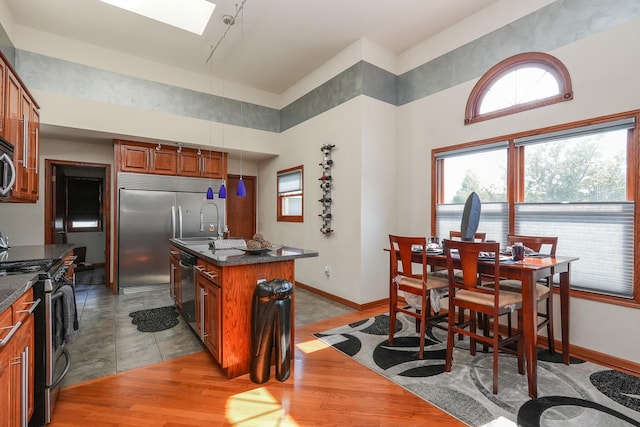 2069 Willow Brook Dr, Bourbonnais, IL 60914 - kitchen featuring stainless steel appliances, dark countertops, a towering ceiling, brown cabinetry, and a skylight