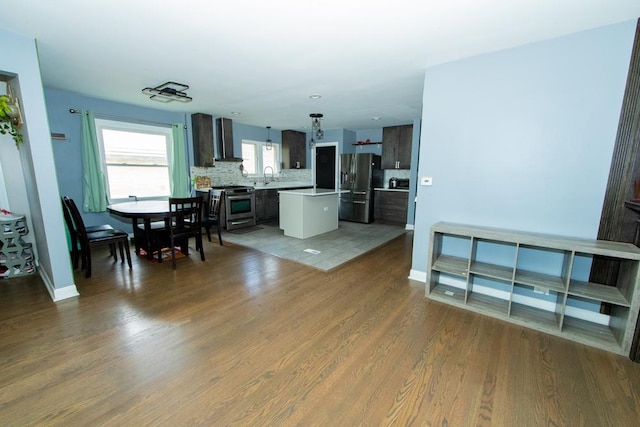 kitchen featuring appliances with stainless steel finishes, wall chimney exhaust hood, a center island, wood finished floors, and light countertops