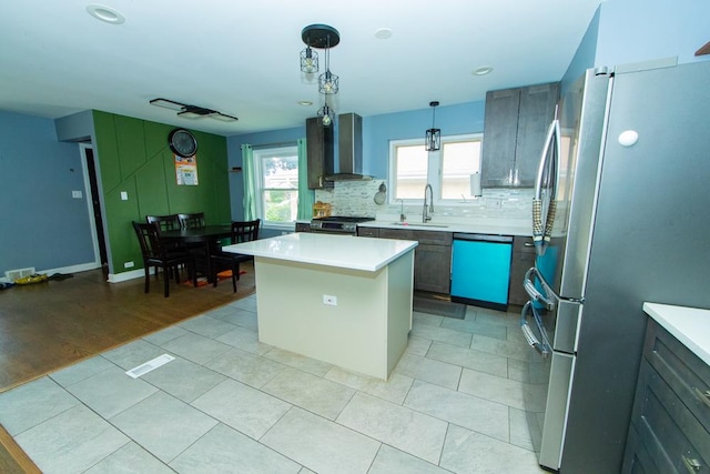 kitchen with stainless steel appliances, wall chimney exhaust hood, backsplash, light countertops, and a kitchen island