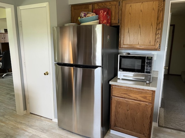 18367 US-150 Hwy, Bloomington, IL 61705 - kitchen with freestanding refrigerator, black microwave, light wood-type flooring, brown cabinetry, and light countertops