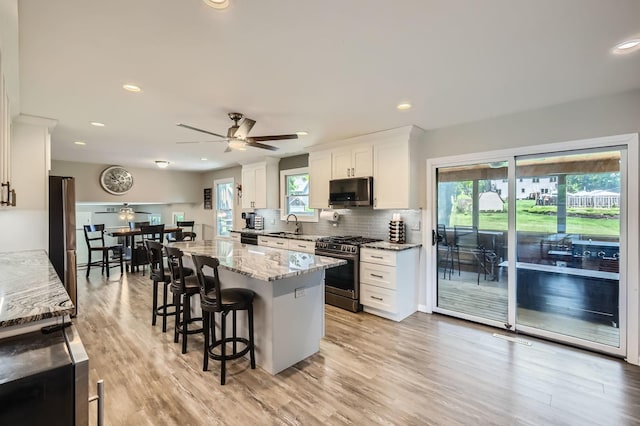 1718 Rosewood Ln, Johnsburg, IL 60051 - kitchen featuring appliances with stainless steel finishes, white cabinets, a kitchen bar, decorative backsplash, and a center island