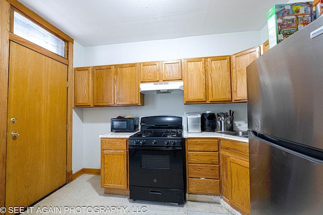 5942 S Calumet Ave, Chicago, IL 60637 - kitchen featuring freestanding refrigerator, black range with gas cooktop, under cabinet range hood, light countertops, and brown cabinetry