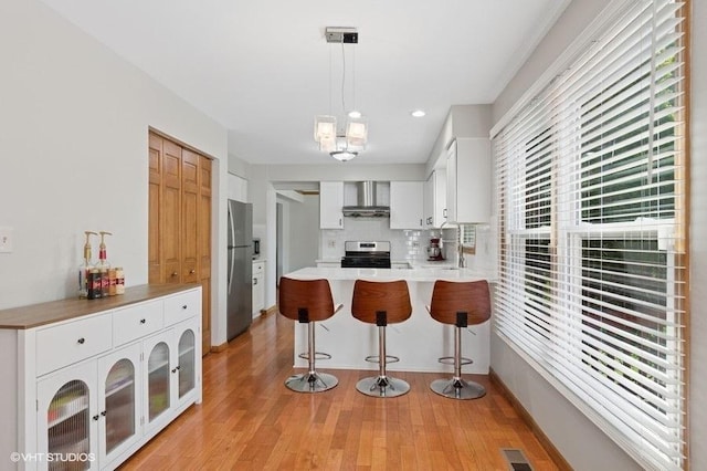 970 E Amberwood Cir, Naperville, IL 60563 - kitchen featuring stainless steel appliances, a peninsula, wall chimney exhaust hood, light wood-style flooring, and recessed lighting