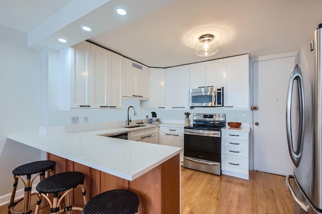 6007 N Sheridan Rd Unit 36F, Chicago, IL 60660 - kitchen with appliances with stainless steel finishes, a peninsula, a breakfast bar area, light wood-style flooring, and light stone countertops