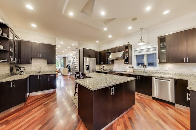 2011 W Huron St, Chicago, IL 60612 - kitchen featuring appliances with stainless steel finishes, under cabinet range hood, backsplash, crown molding, and a kitchen breakfast bar