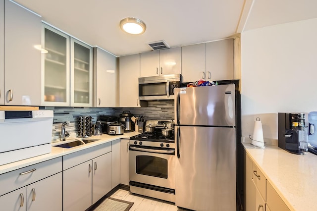 5100 N Sheridan Rd Unit 410, Chicago, IL 60640 - kitchen with appliances with stainless steel finishes, decorative backsplash, gray cabinetry, glass insert cabinets, and light wood-style floors