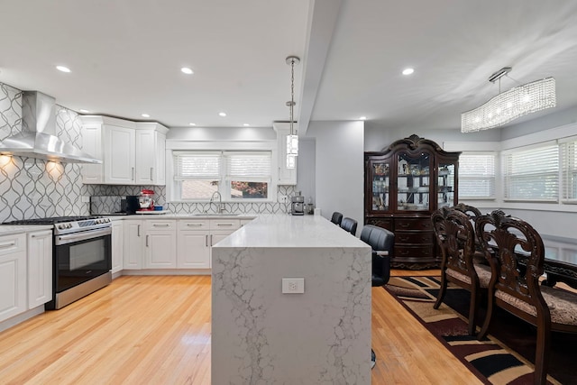 8313 W Ballard Rd, Niles, IL 60714 - kitchen featuring gas range, wall chimney exhaust hood, a peninsula, light wood-style floors, and decorative backsplash