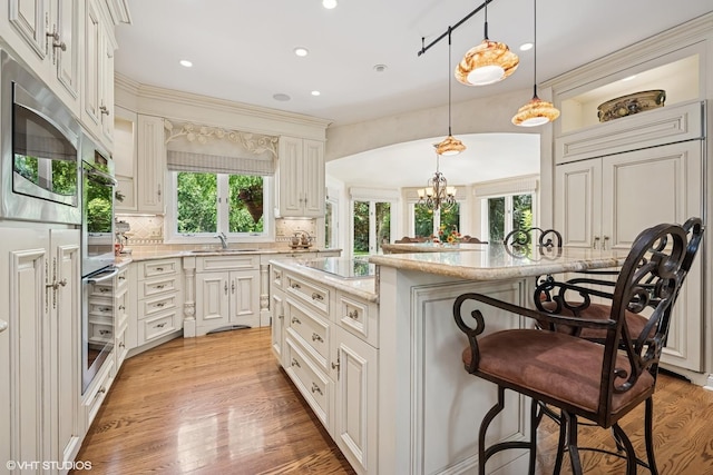 85 Ela Rd, Inverness, IL 60067 - kitchen featuring a breakfast bar, appliances with stainless steel finishes, backsplash, light wood finished floors, and light stone counters