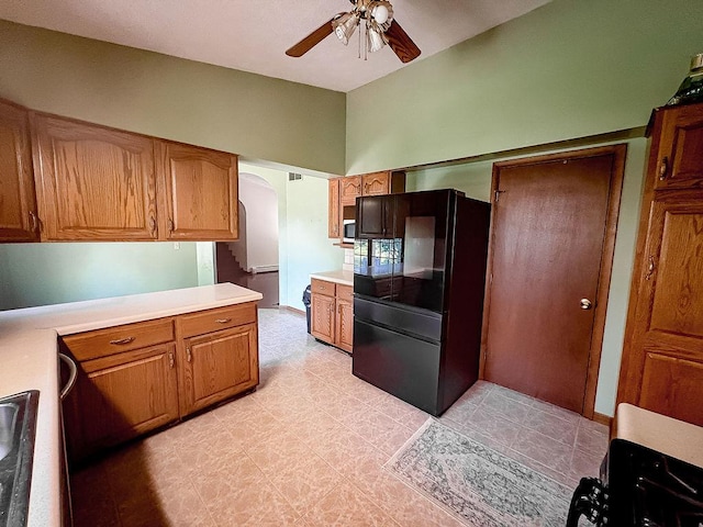 202 E 8th St, Gridley, IL 61744 - kitchen with freestanding refrigerator, arched walkways, a ceiling fan, light countertops, and brown cabinetry