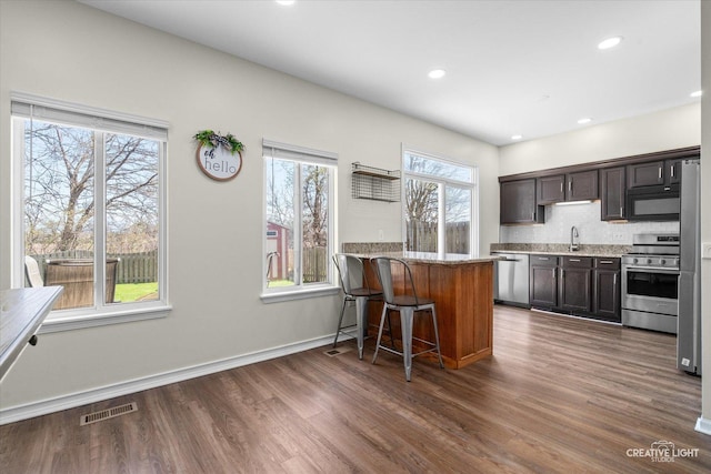 307 Gregory Ln, Plano, IL 60545 - kitchen with stainless steel appliances, dark wood-type flooring, dark brown cabinetry, a breakfast bar, and light stone countertops