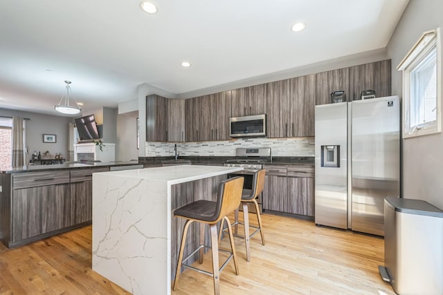 641 S Maple Ave Unit I, Oak Park, IL 60304 - kitchen featuring stainless steel appliances, a center island, backsplash, a kitchen bar, and light wood-style flooring
