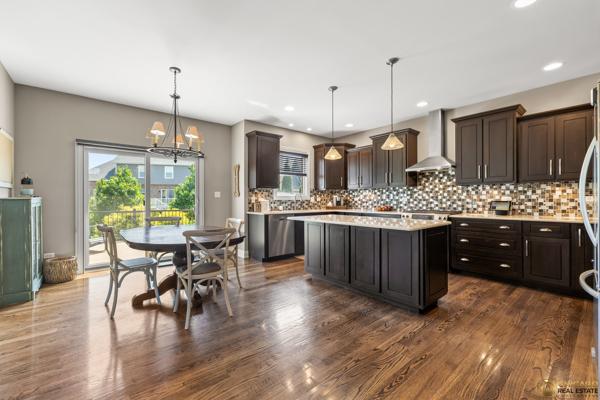 13119 Kinsale Ct, Lemont, IL 60439 - kitchen with wall chimney range hood, light countertops, a kitchen island, tasteful backsplash, and dark brown cabinets