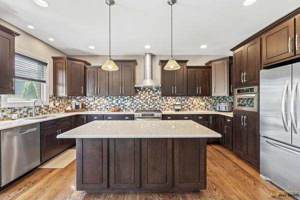 13119 Kinsale Ct, Lemont, IL 60439 - kitchen featuring appliances with stainless steel finishes, wall chimney exhaust hood, dark brown cabinetry, a kitchen island, and recessed lighting