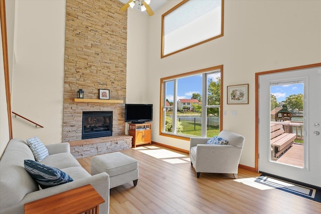 3220 Weeping Cherry Dr, Champaign, IL 61822 - living room featuring a stone fireplace, light wood-type flooring, a towering ceiling, and a ceiling fan