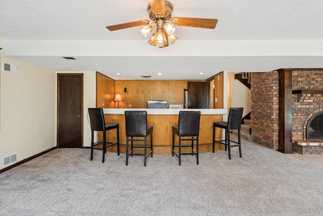 13115 Maple Rd, Mokena, IL 60448 - kitchen featuring carpet flooring, a ceiling fan, a textured ceiling, a kitchen bar, and a fireplace